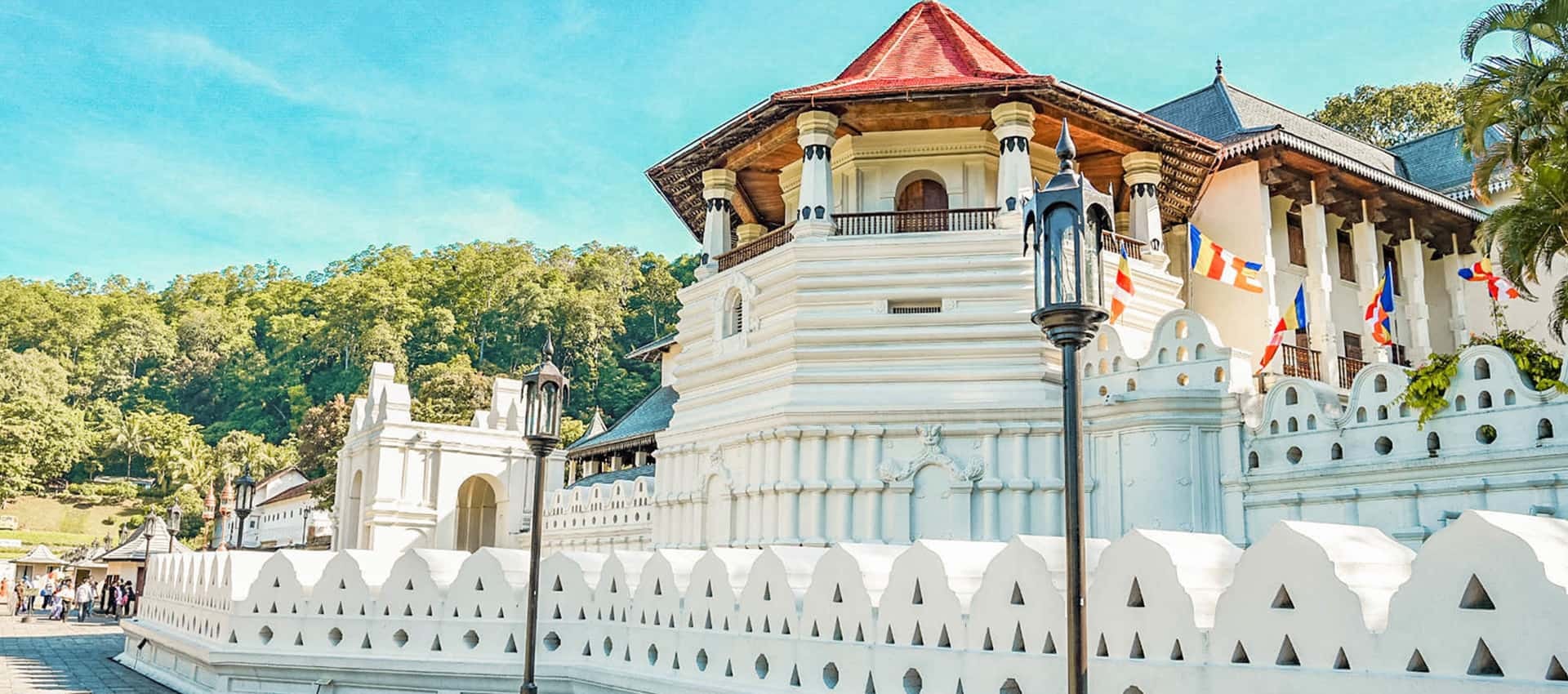 The building is white with a red-tiled roof and features a distinctive white wall with pointed carvings.